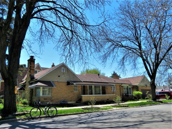 A tour bike at front of a mid century yellow brick corner one story home with the entrance on the long side.