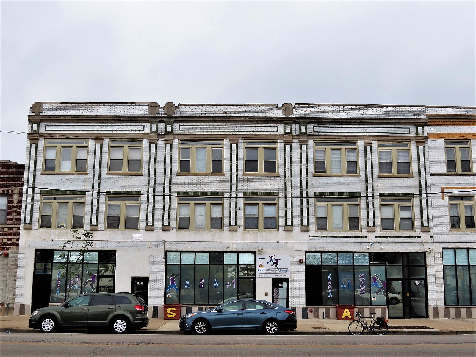 A tour bike at front of three identical green and white glazed brick three story storefronts.