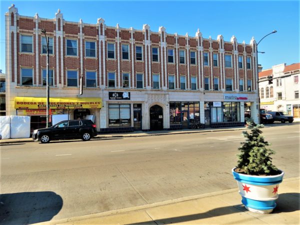 A tour bike leaning on a corner block terra cotta covered three story storefront and flat style former bank building.