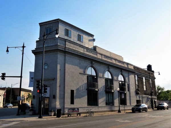 A tour bike next to a three street intersection corner two story limestone Classical Revival former bank building.