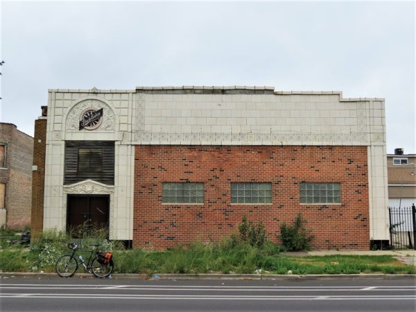 A tour bike at front of a bricked up motor showroom window framed with cream terra cotta and a Studebaker trademark wheel above the door.