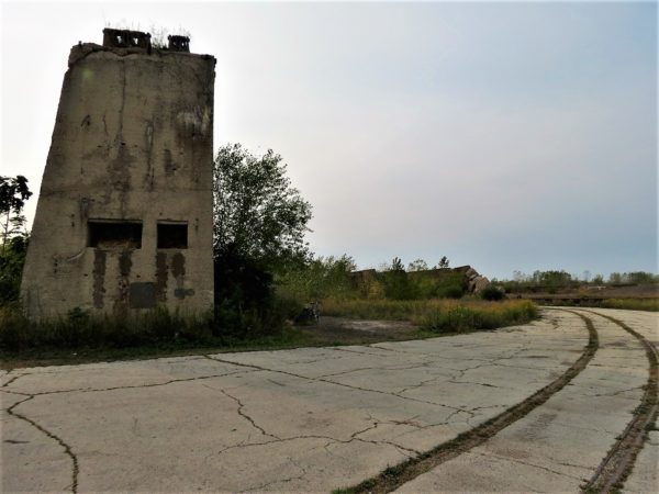 A tour bike leaning against a massive concrete former ship slip covered in weeds with train rails sweeping in front the front right and curving out of frame.