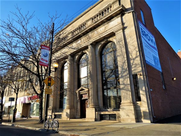 A tour bike at fton of a two story single lot Classical Revival former bank with three large arched two story windows.