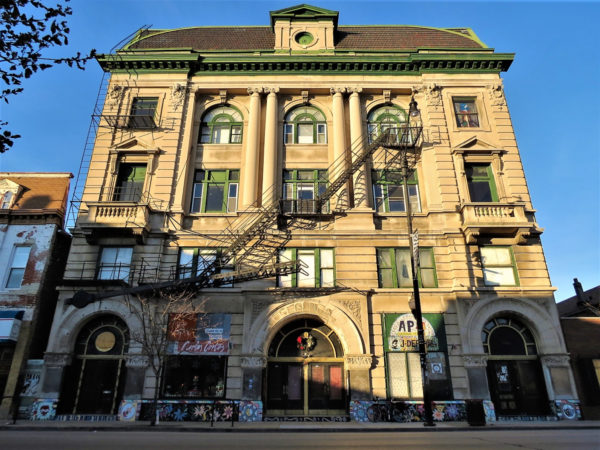 A tour bike leaning on a triple lot Classical Revival limestone four story with a mansard roof and dormer.