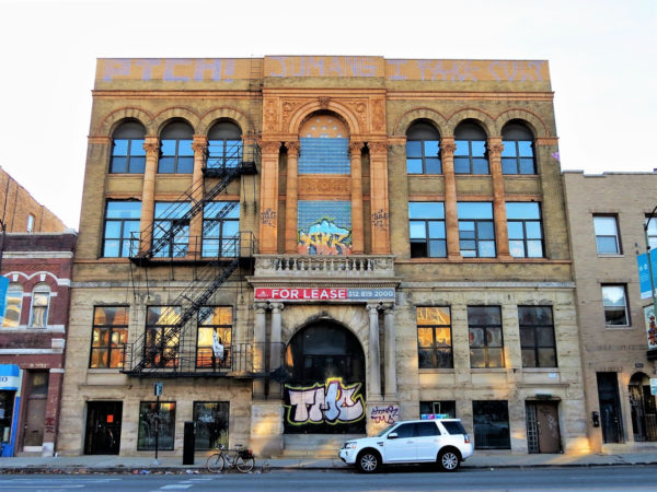 A tour bike at front of four story double lot building with a façade of wide widows, limestone covered first and second floor and light brown terra cotta covered third and fourth.