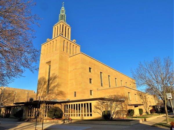 A tour bike at front of a Mid-century Art Deco mix yellow smooth limestone church with center entrance and tower.