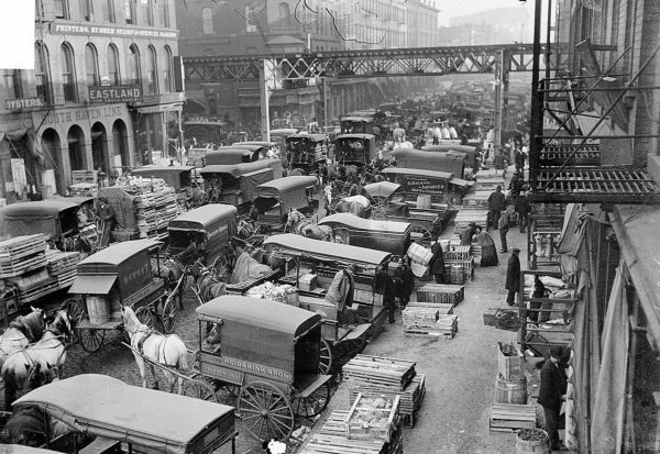 A turn of the century historic black and white of a market street jammed filled of wagons facing each other leaving a small path