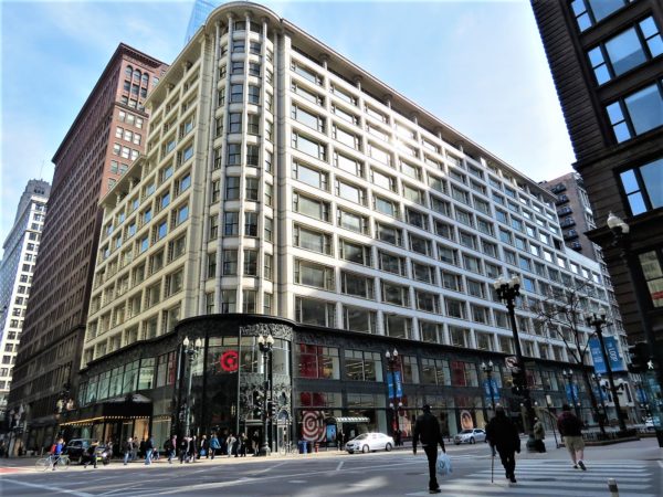 A tour bike leaning below an eleven story cream Chicago School corner department store building with first floor intricate floral design in black metal.