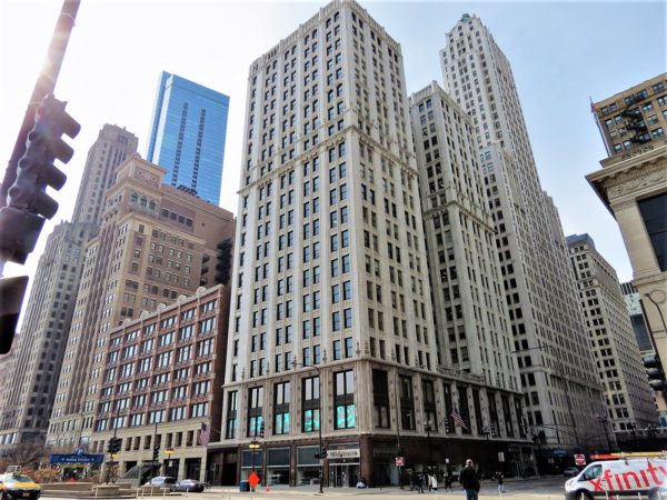 A tour bike barely visible below a cream colored 20 story corner building with brown granite first and second floors.