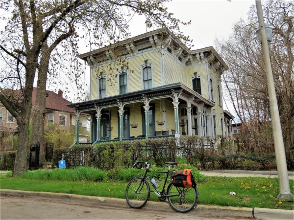 A tour bike at front of a yellow and white wood two story Italianate single family home.