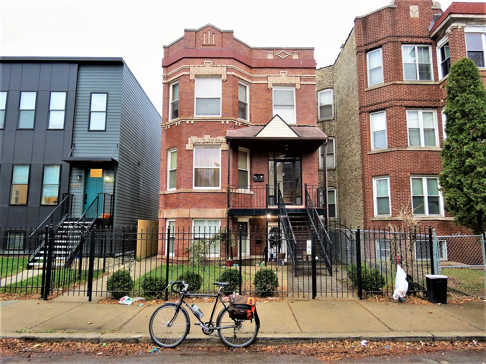 A tour bike at front of a red brick three flat with tan brick design accents around the windows and roofline..