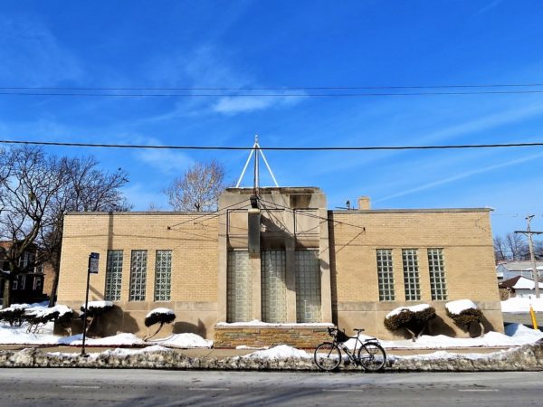 A tour bike at front of a one story yellow brick Art Deco funeral parlor.