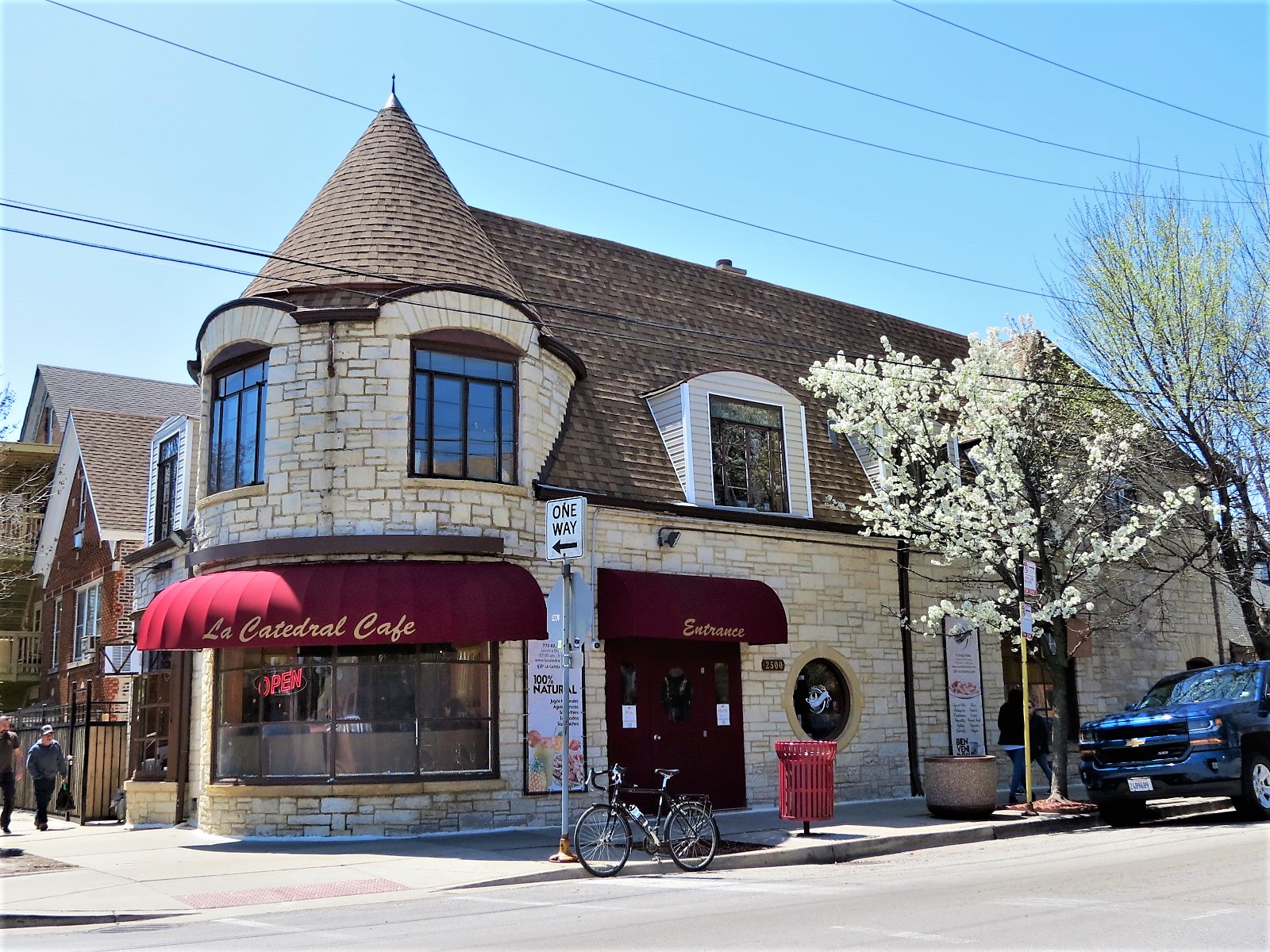 A tour bike standing at front of a stoner clad Tudor Revival corner building with cone capped turret and an ocular window on the side.