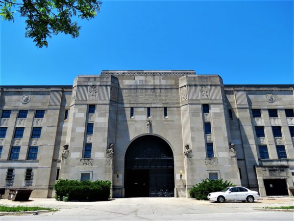 A tour bike leaning on the large brown wood bay door of a large mass Art Deco limestone building with military themed design details.