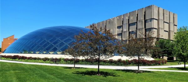 A tour bicycle standing at front of the Mansueto Library, a glass dome that rises from the ground and the Regenstein Library, three story windowless concrete Brutalism.