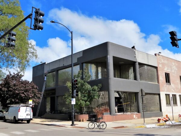 A tour bicycle in front of a two story mid century front with glassblock windows curved on the corner.