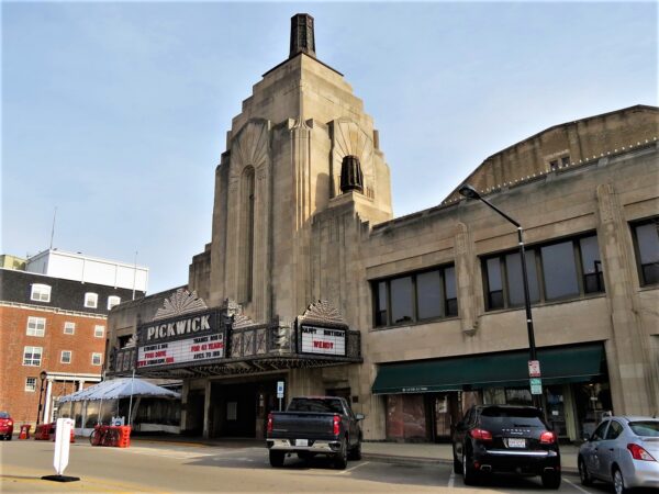 A tour bike standing at front of a limestone Art Deco movie theatre with a central three story Art Deco tower.