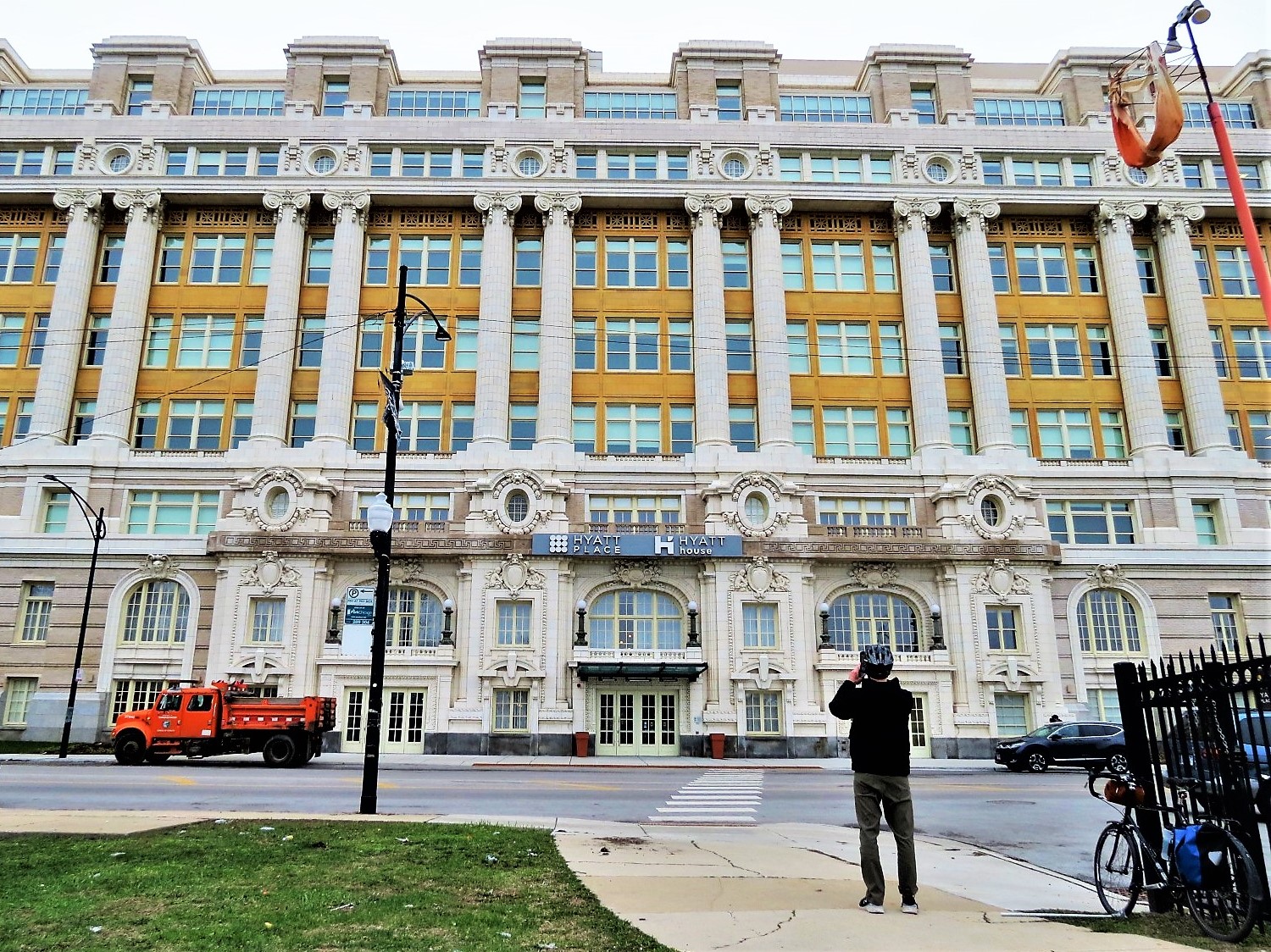 A CBA bike tour rider taking a picture of the large mass Beaux Arts style old Cook County Hospital, restored as Hyatt Place hotel.