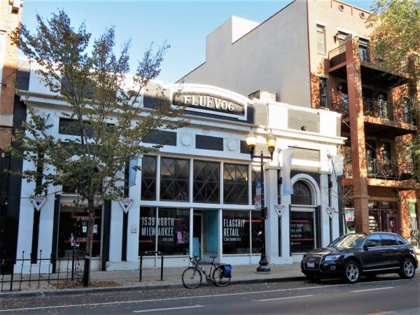 A tour bicycle standing at the curb in front of a one story storefront painted black and white with two arched entries on either side of a glass front.