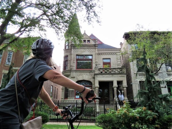 A CBA bike tour ride from the back looking at a limestone Queen Anne single family home with corner turret.