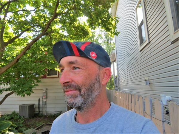 A handsome man with a salt and pepper beard and blue cycling cap looking away from the camera, wink.