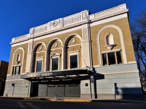 A tour bike standing at front of a yeloow brick and white terra cotta detailed Classical Revival / Beaux Arts 1920s movie theater.