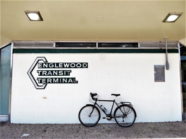 A tour bike leaning on a white painted wall with a mid-century style metal sign reading Englewood Transit Terminal.