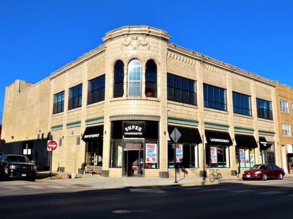A tour bike standing to the side of a two story terra cotta covered and wide widows on both stories 1920s car showroom, now laundromat.