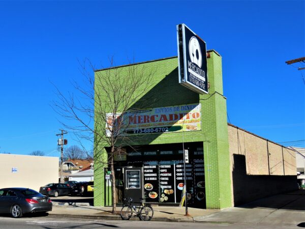 A tour bike standing at front of a single lot one story store front with a pronounced green glazed brick two story façade.