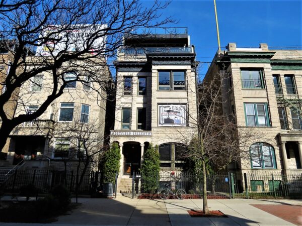 A tour bike leaning on the front black metal fence of a greystone three flat with stadium seating on the roof.