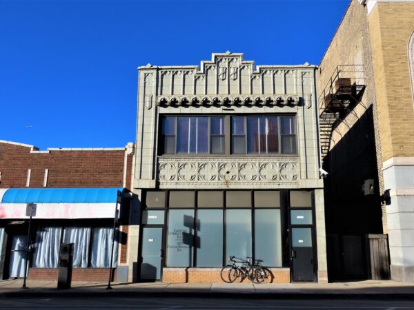 A tour bike leaning on a two story storefront and flat with a terra cotta second floor with quatrefoil and corbeau designs 
