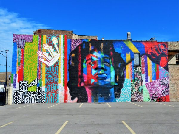 A tour bike leaning on a vibrant colored mural of a Afroed young black man looking skyward surrounded by symbols of power and uplift.