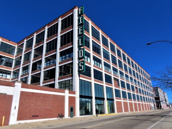 A tour bike leaning on the red brick of a massive six story wide window box former 1930s era factory now lofts. 