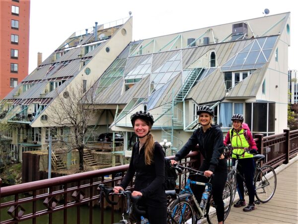 Three CBA bike tour riders looking at the camera with a nautical themed Post-Modern building behind.