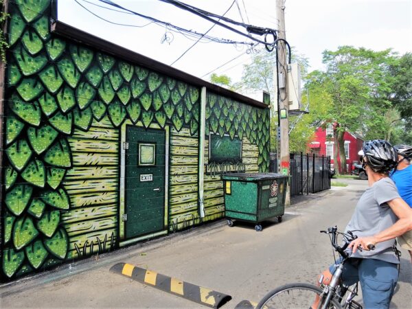 Two CBA tour riders looking at an alley mural showing the "back door" of the building done in different shades of green dots.