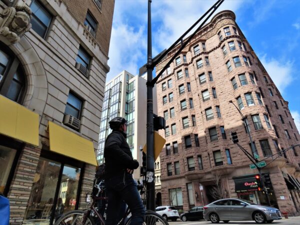 A CBA tour rider in silouette looking at an eight story late 19th century corner Queen Anne apartment building.