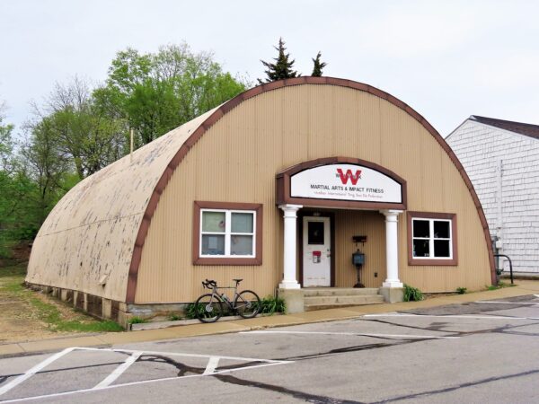 A tour bike standing out from of a arched tan painted corrugated metal building with two white columns framing the entry.