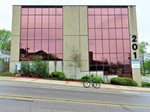 A tour bike standing at front of a three story pink glass mid-century office building sitting on a steep hill.
