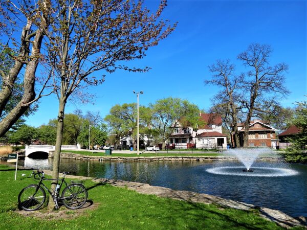 A tour bike leaning on a tree with a lagoon and fountain behind and Queen Anne homes on the other side.