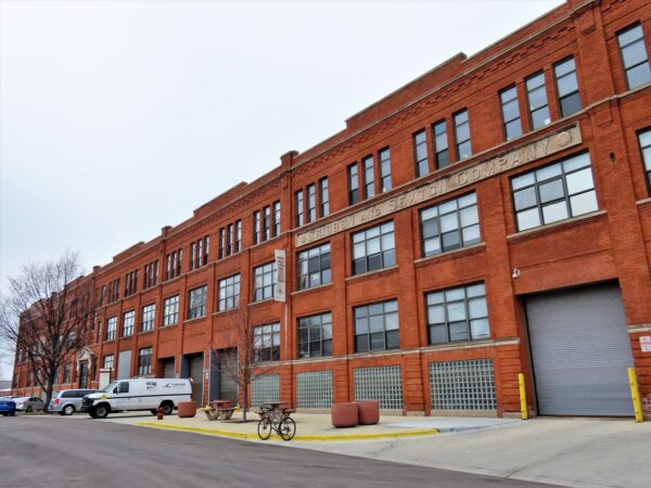 A bicycle standing in front of a red brick three story early 20th century factory building.