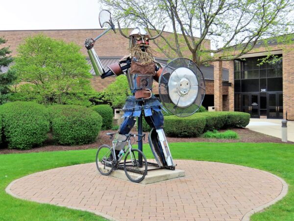 A tour bicycle leaning on a Viking sculpture made of welded together metal bike and car parts. 