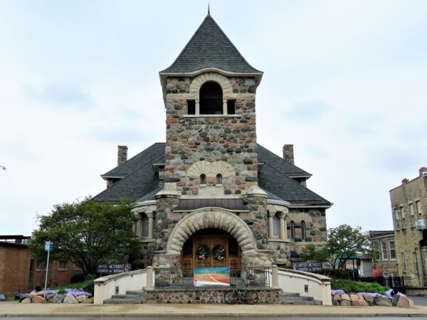 A tour bike standing at front of a grey cobble stone Romanesque church with a large limestone arch entry and central bell three story tower.