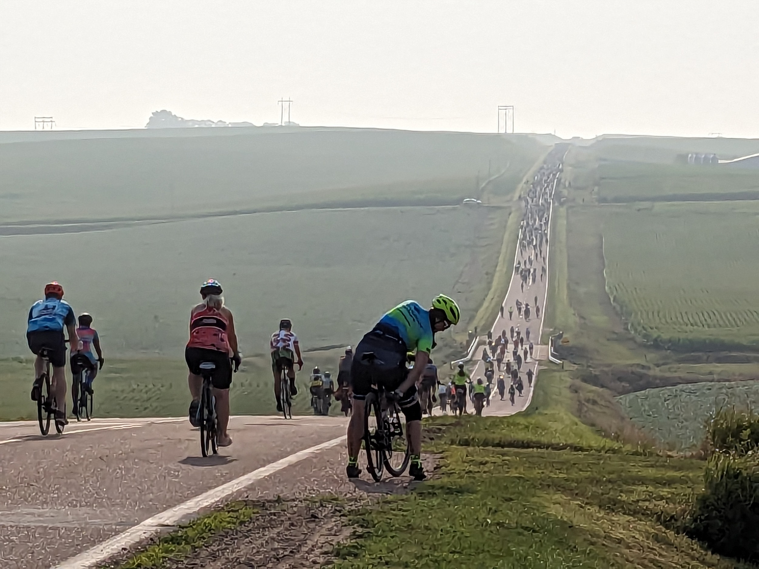 A large muber of cyclists going down then up a hill in the rural distance.