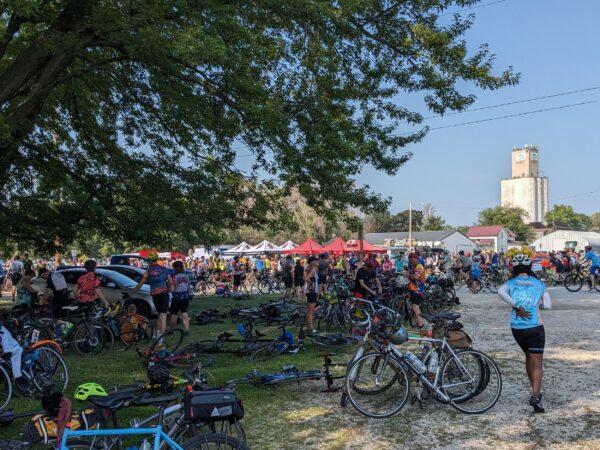 A large number of bikes in the shade with a white grain elevator in the back.