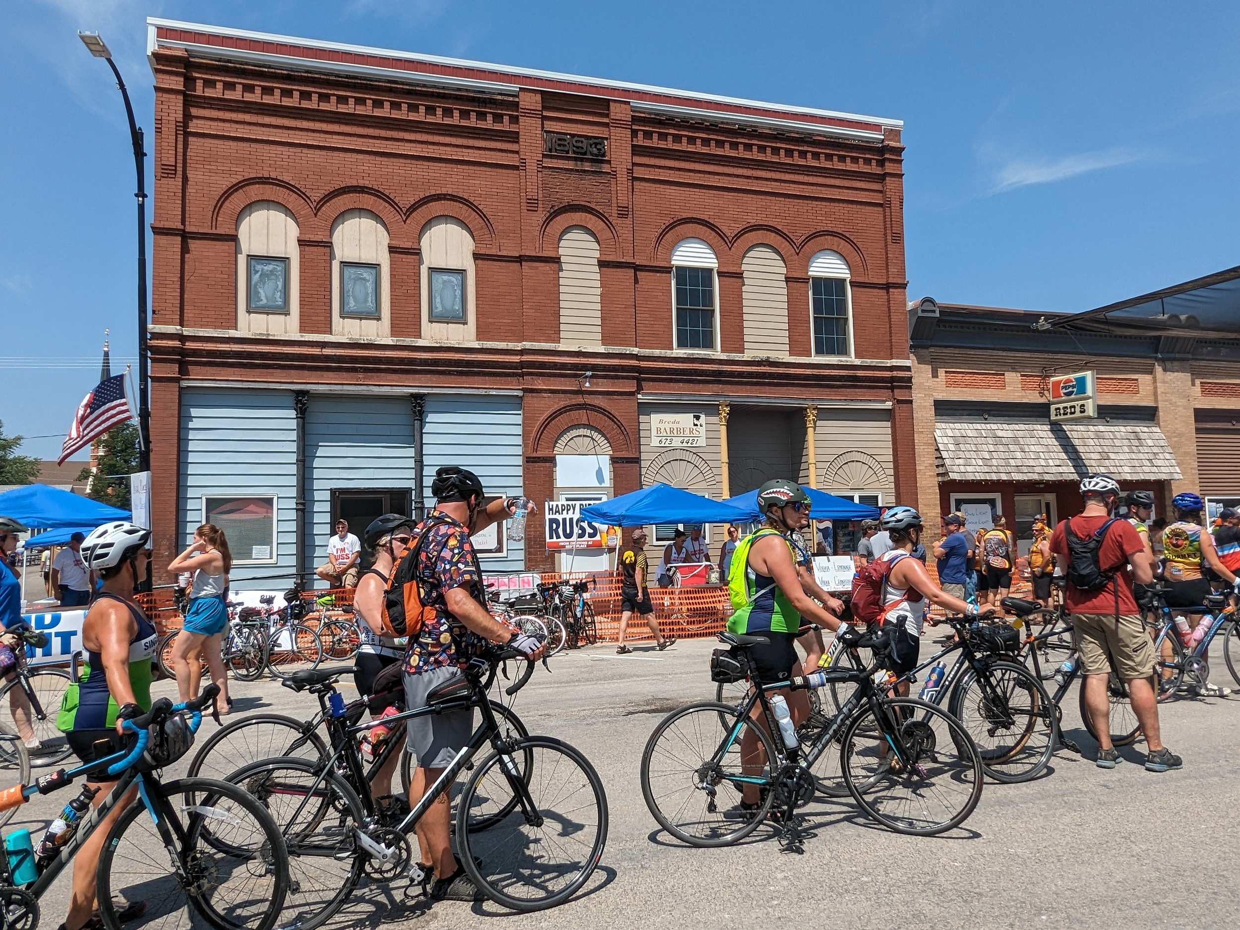 Cyclists walking their bikes past a two story brown brick storefront.