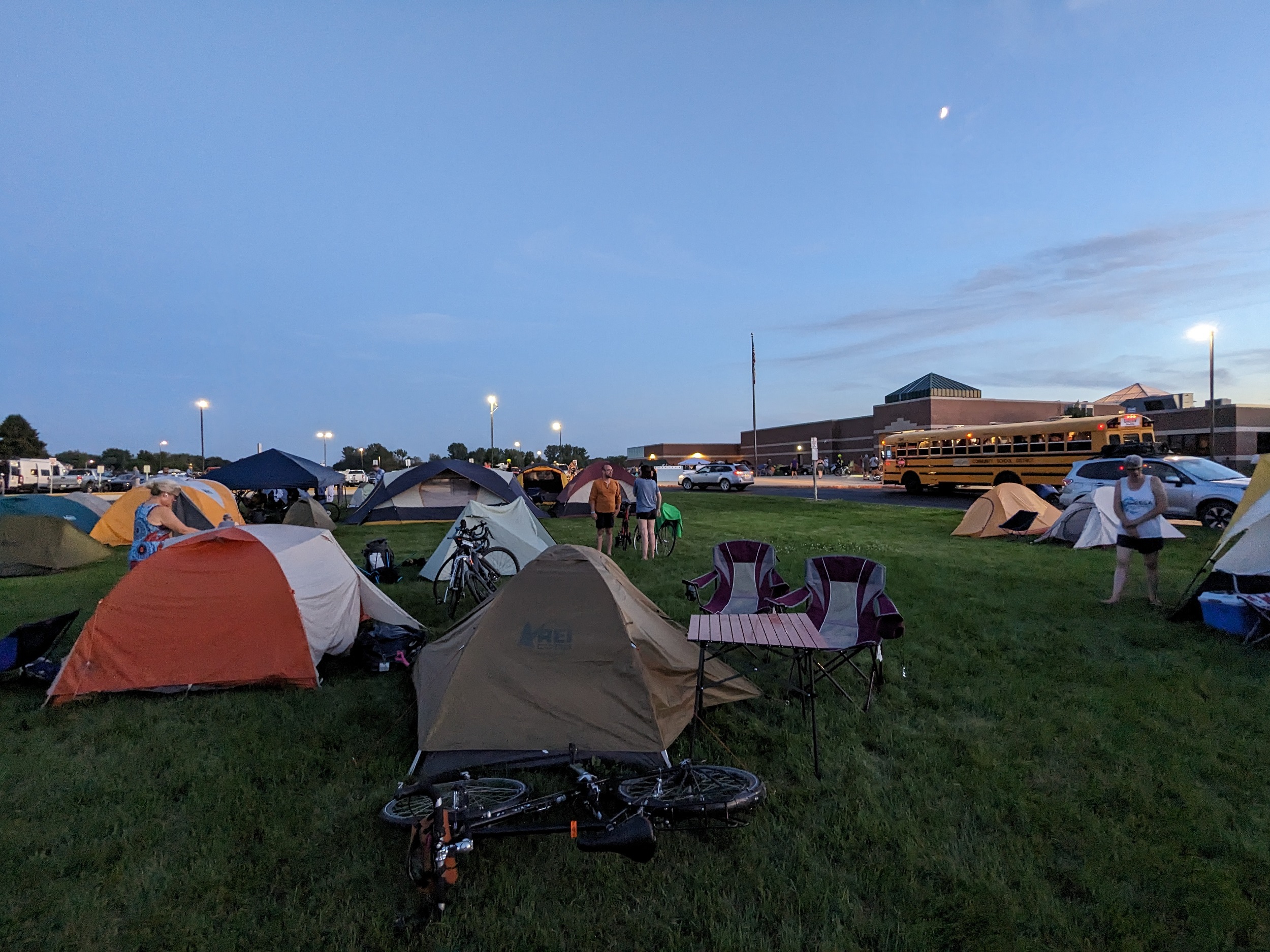 Many tents in a field with a high school building behind.