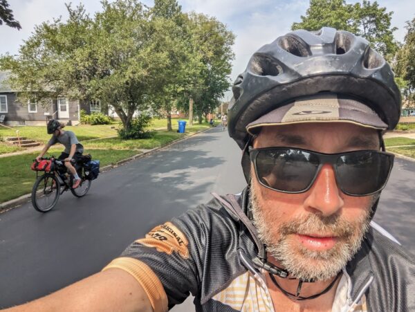 Me in an action selfie with another bike rider to my right and a tree lined street.