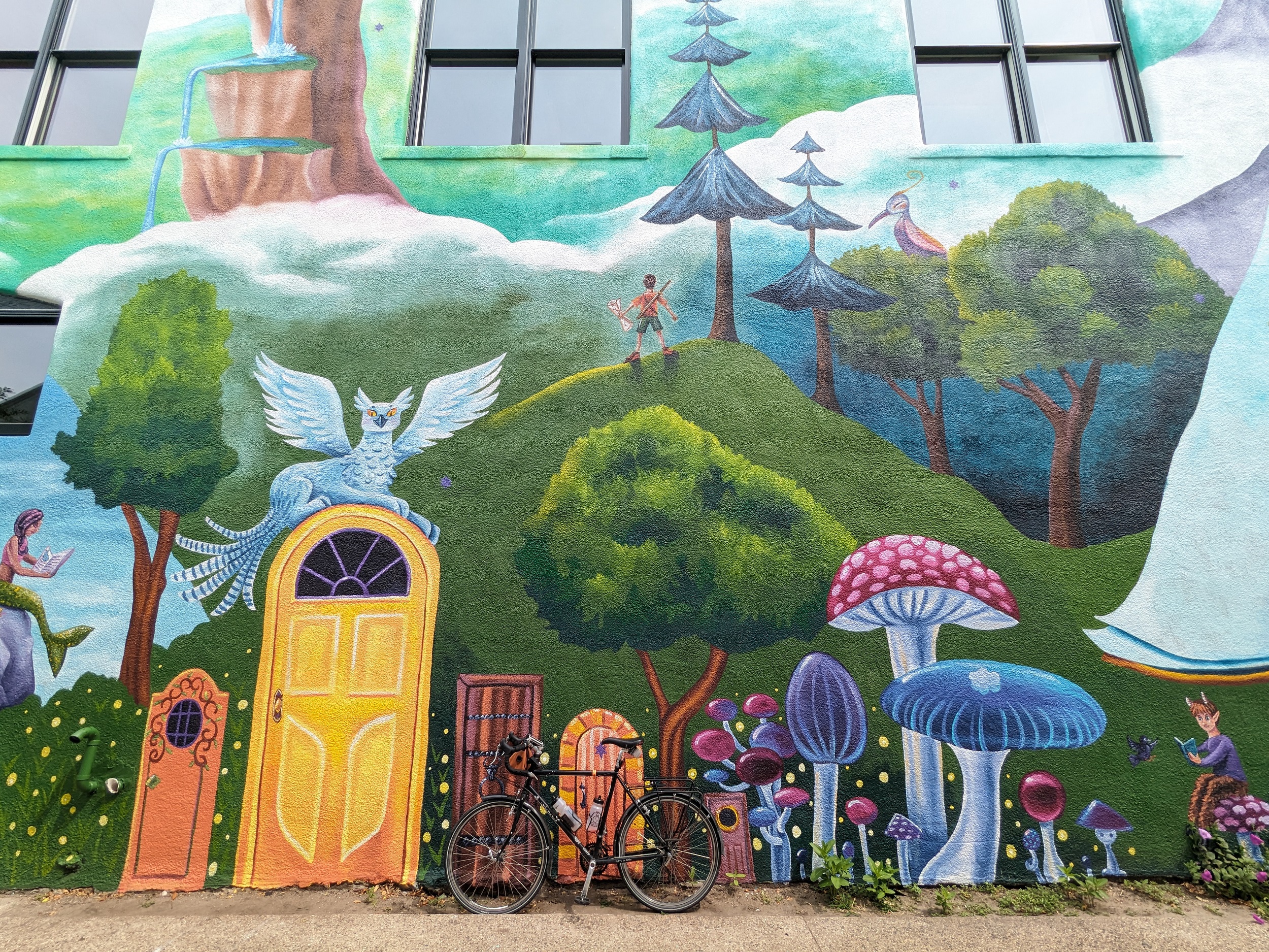 A tour bike leaned against a fantiastical themed mural with a boy on a hill with arms outstretched.