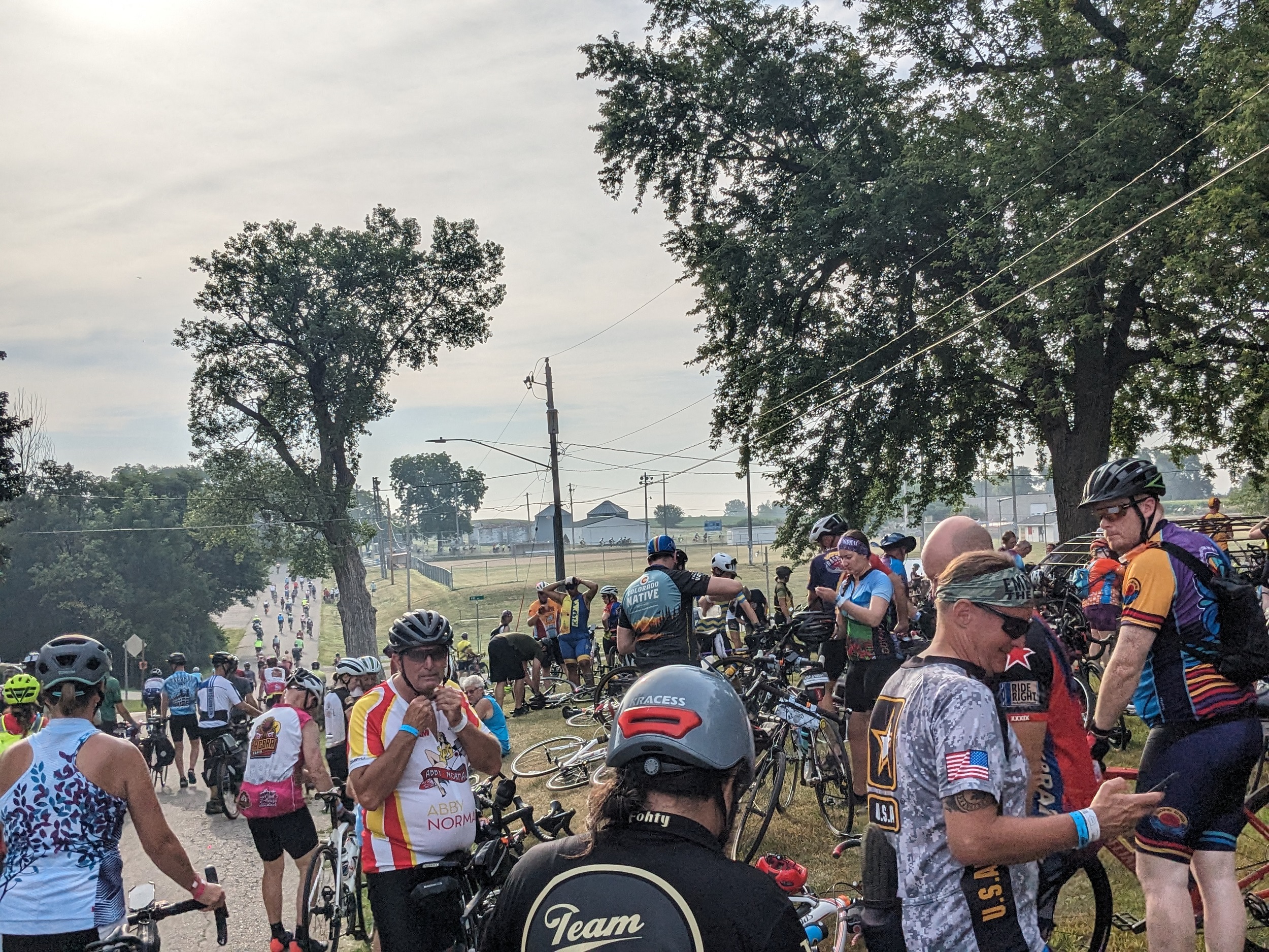 A crowd of cyclist extending into the distance on a downhill then crossing the picture to the right.