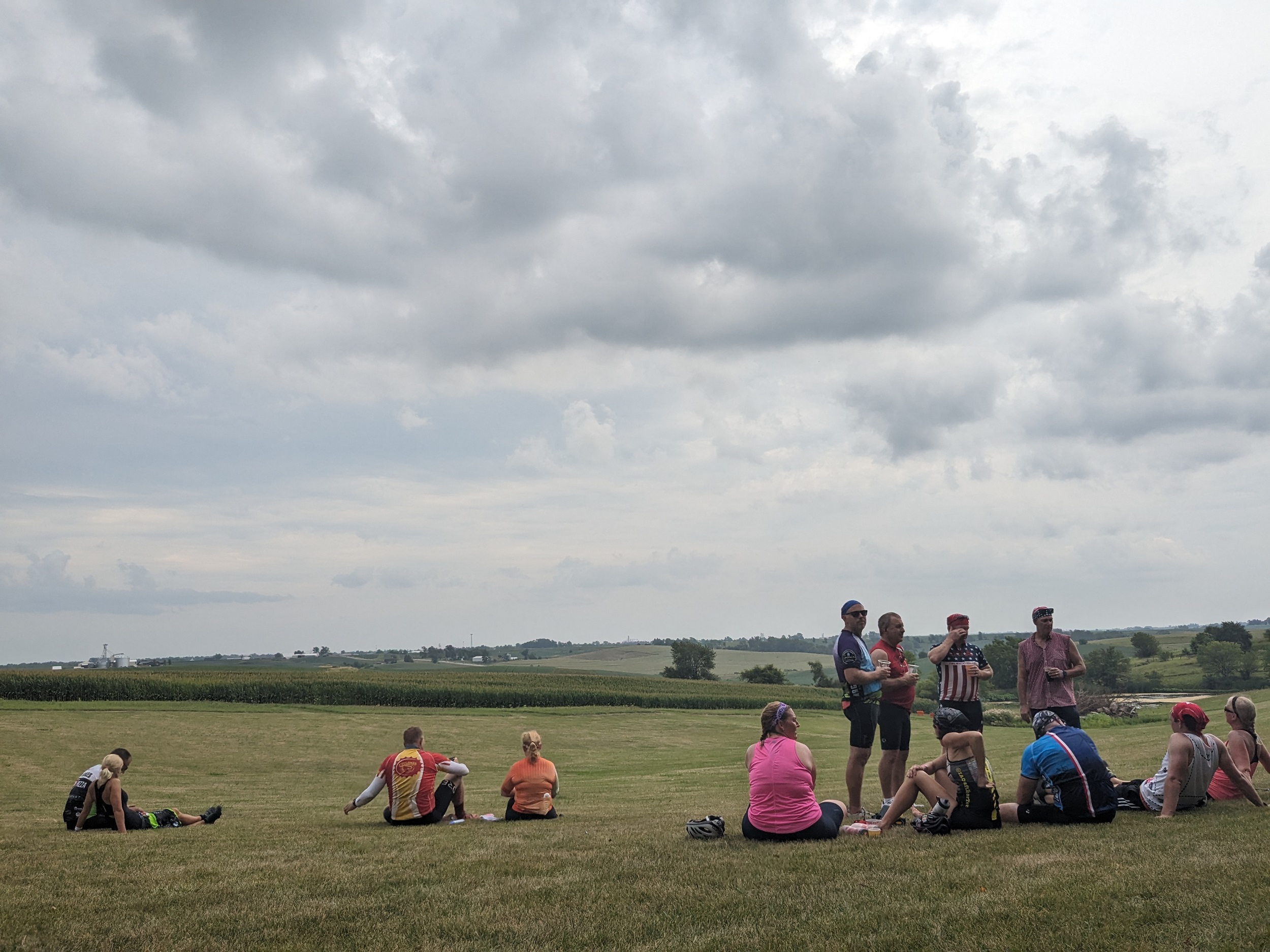 small gathering of cyclists talking and drinking beer with fields extending in the distance.